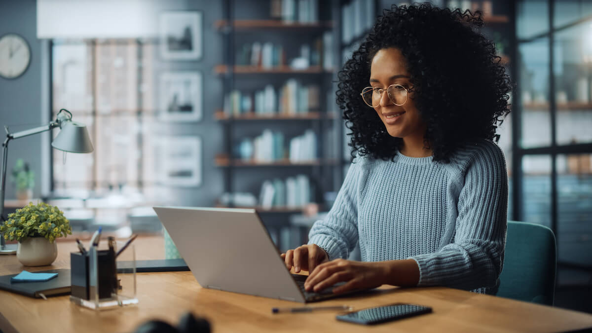 Latina female Sitting at a desk in a living room and using laptop computer at home