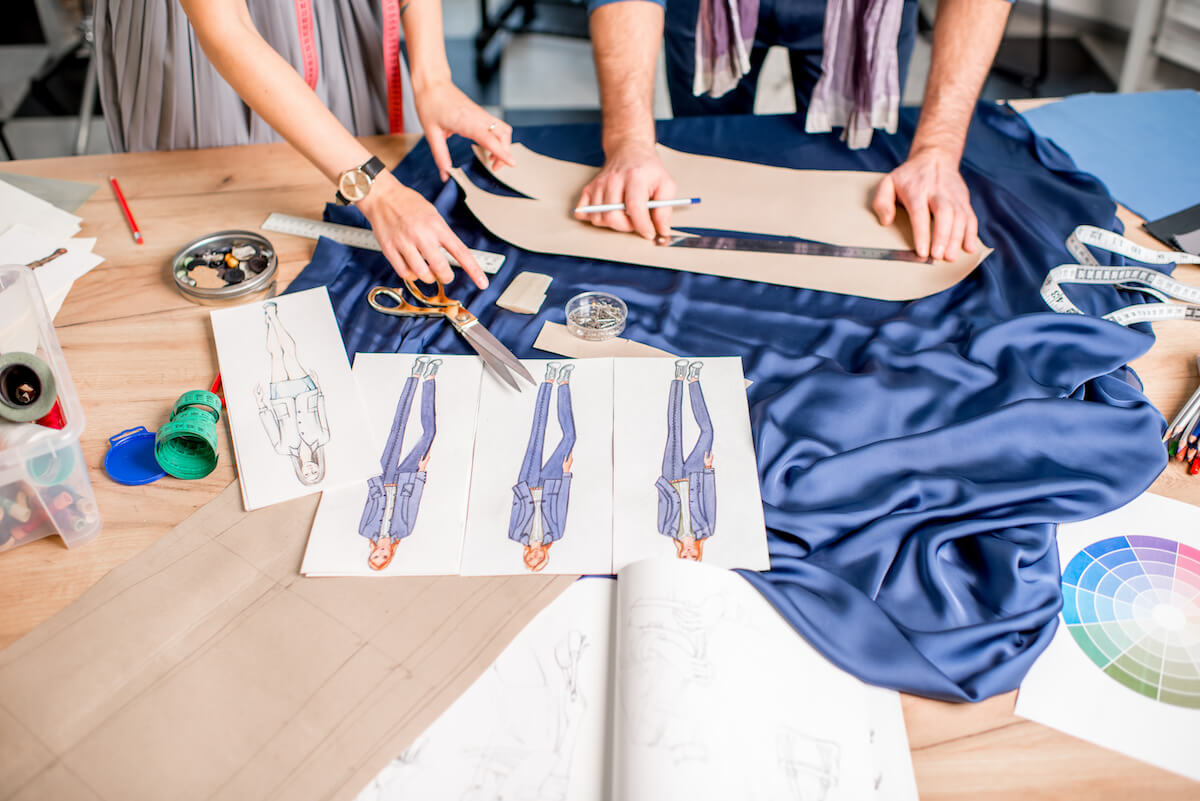 Cutting blue fabric on the table full of tailoring tools.