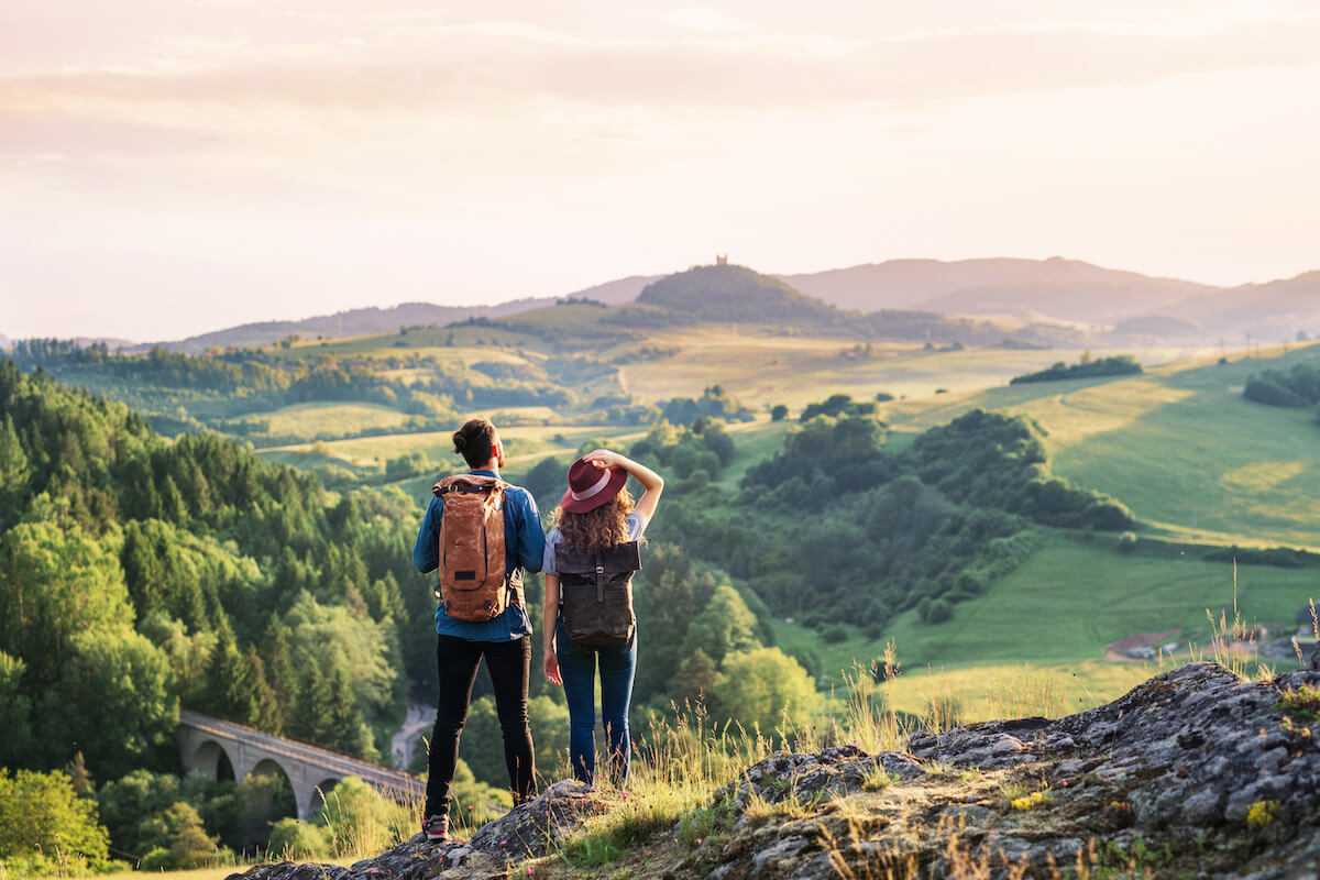 Rear view of young tourist couple travellers with backpacks hiking in nature, resting.