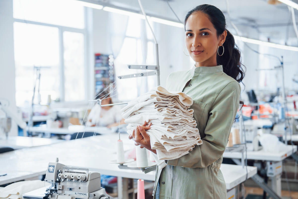 Woman dressmaker stands in the factory with cloth in hands.