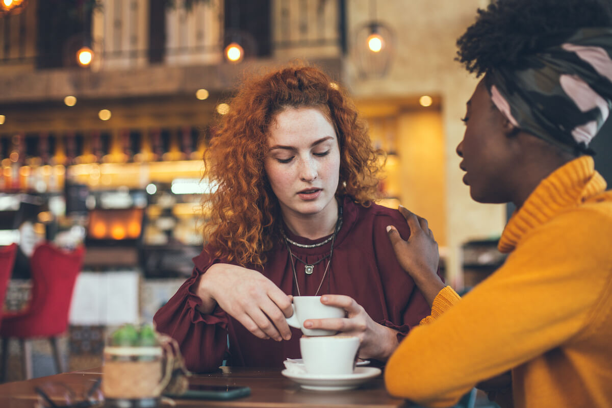 A young woman is talking with a female friend about her problem in a cafe. 