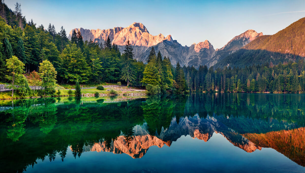 Calm morning view of Fusine lake. Colorful summer sunrise in Julian Alps with Mangart peak on background, Province of Udine, Italy, Europe.
