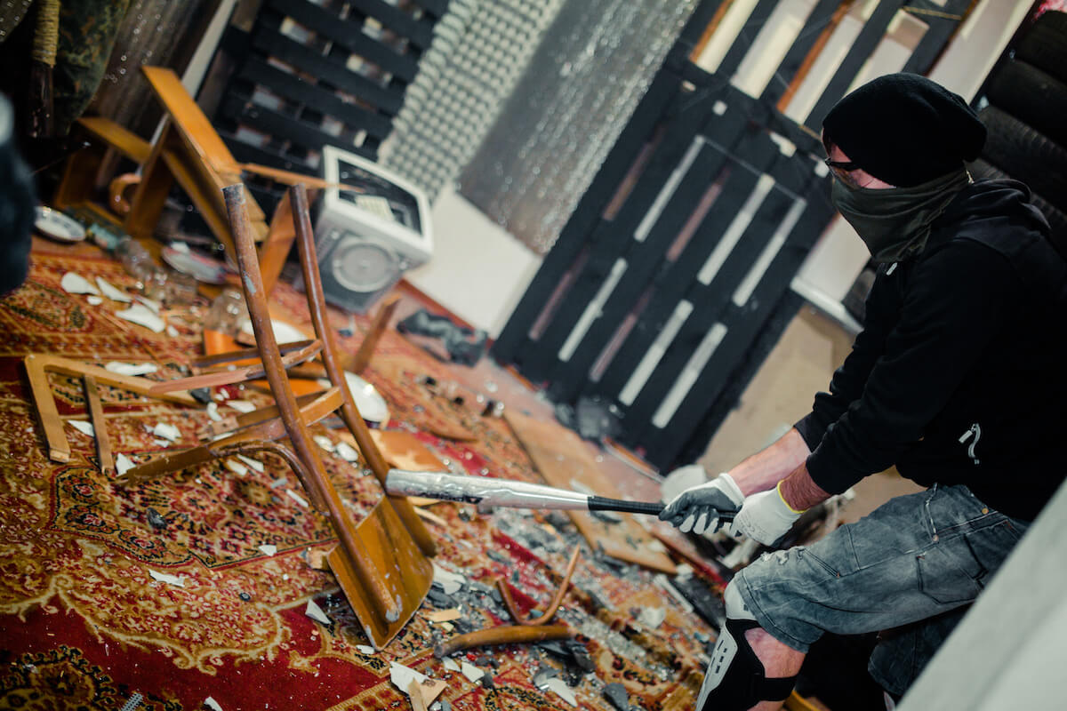 Man in the rage room smashing chair and old computer with a baseball bat