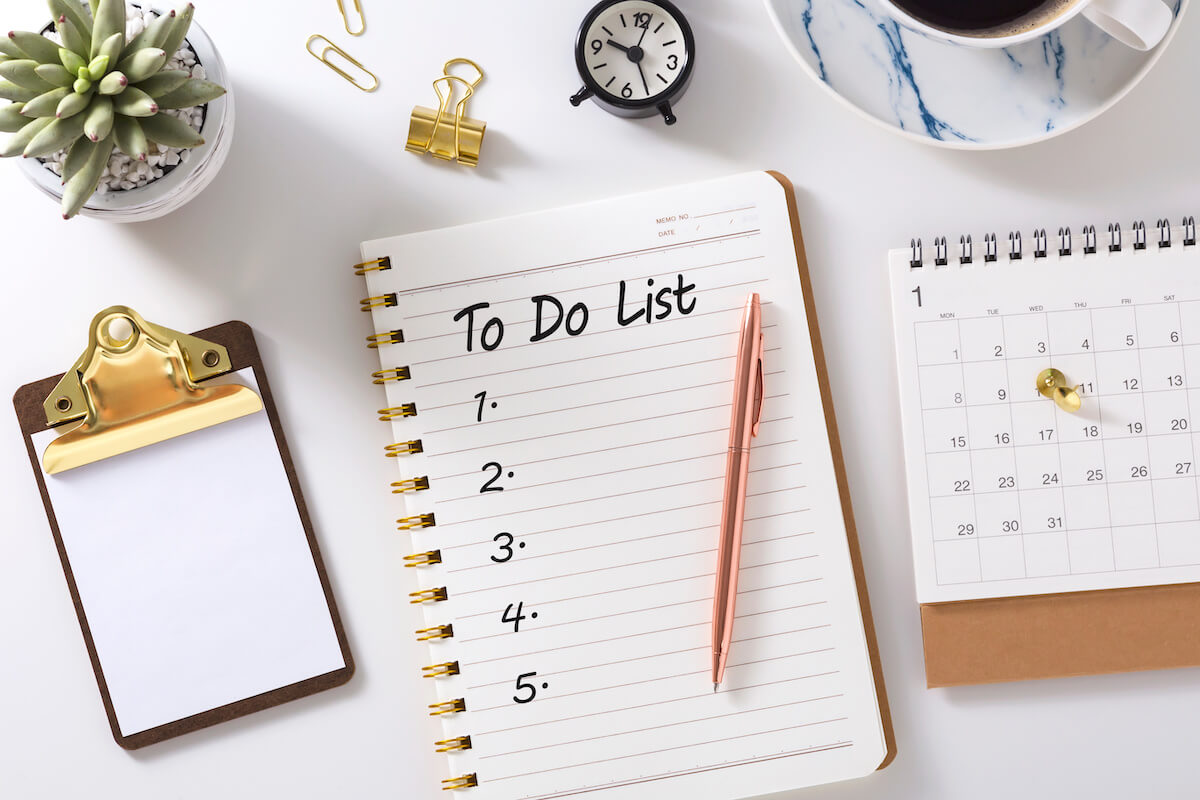 To do list in notebook with calendar,  clock and clipboard on white desk, top view