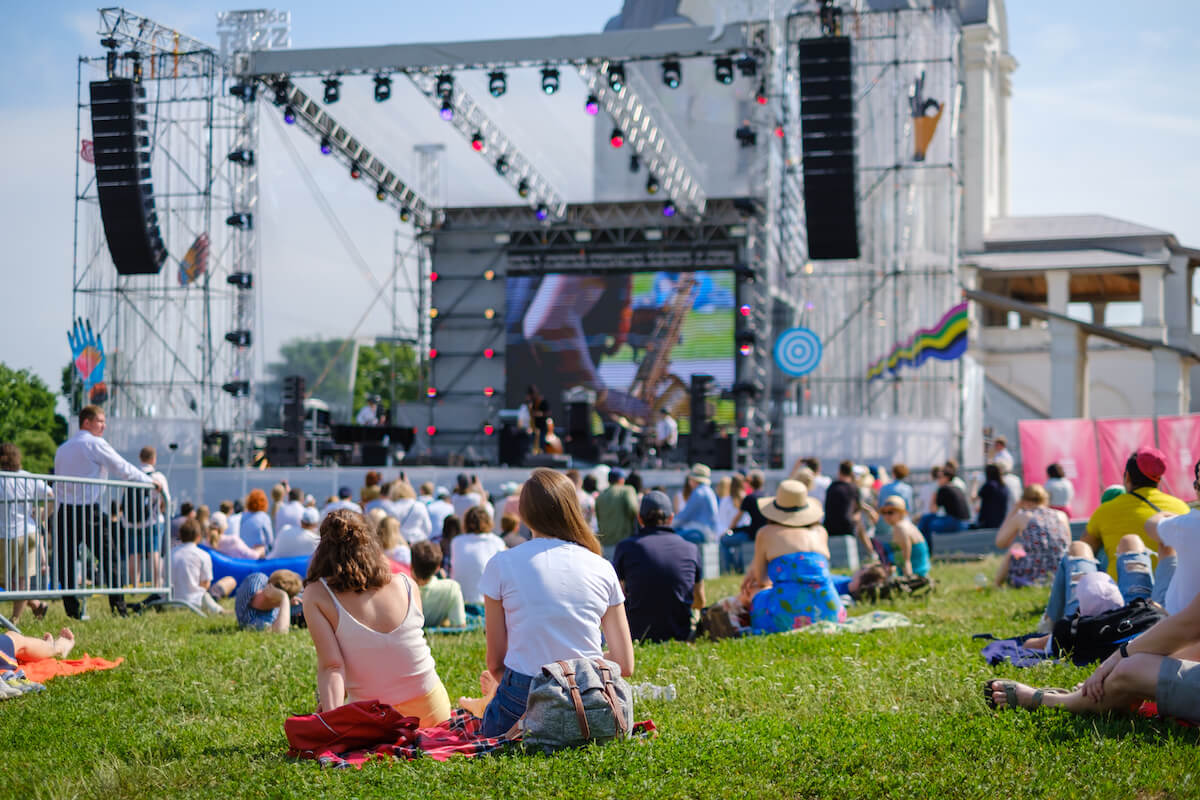 Girls friends watching concert at open air music festival, back view, stage and spectators at background