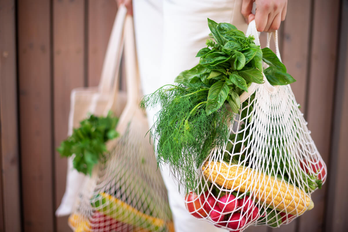 Woman holding cotton shopper and reusable mesh shopping bags with vegetables, products. 