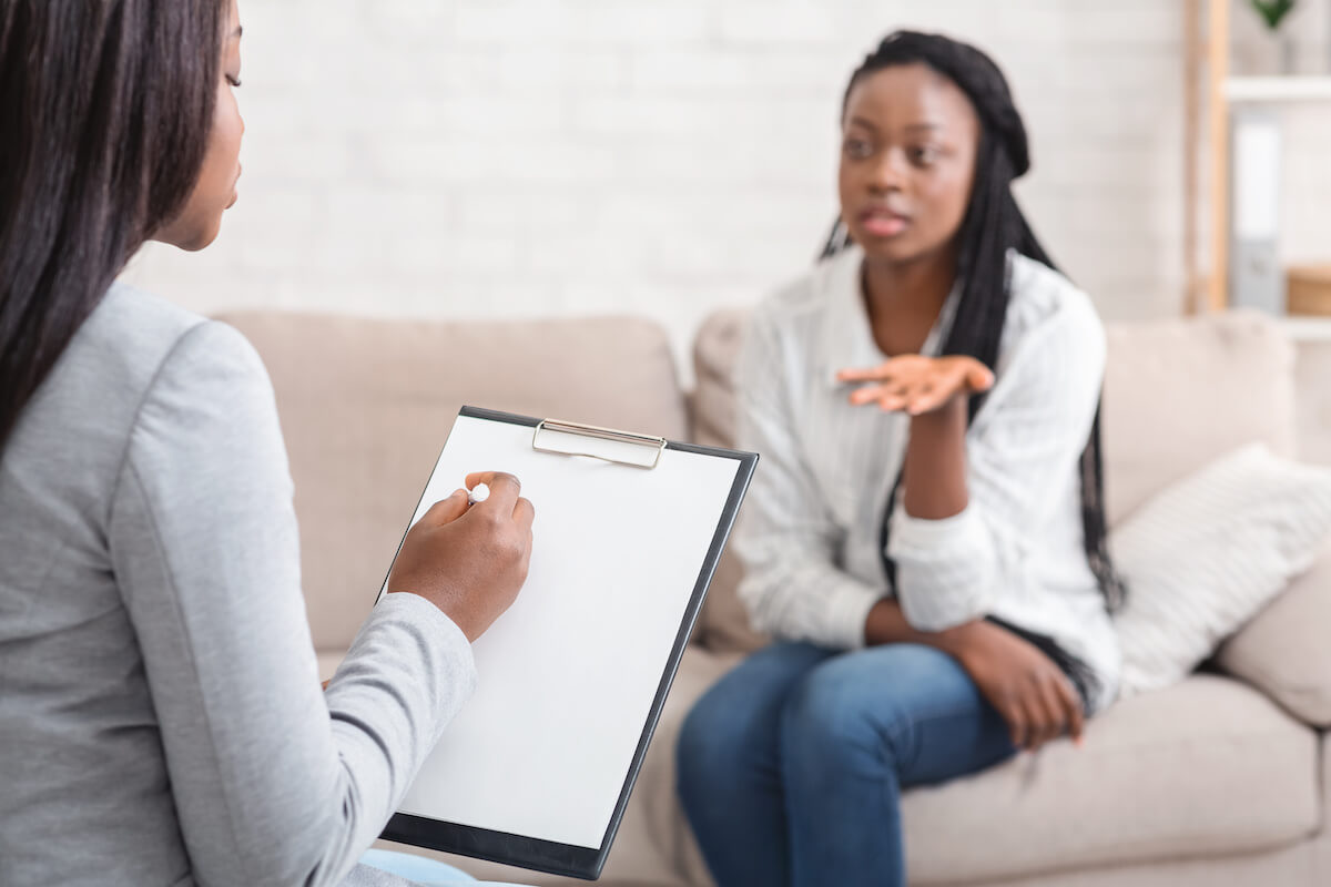 Psychologist taking notes during therapy session with her emotional female patient that talking with about her problems and actively gesturing