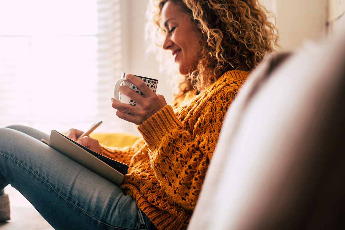 Woman at home write affirmations on a diary while drinking a cup of tea.