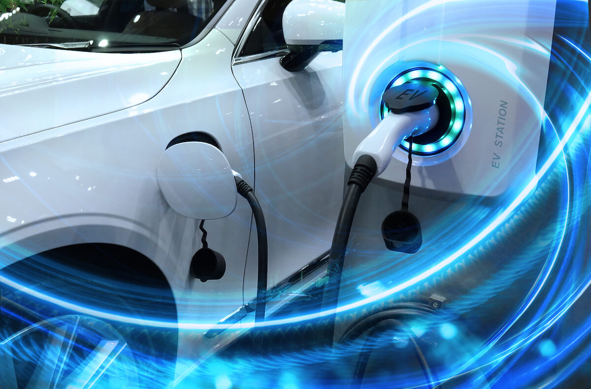 EV Car or Electric vehicle at charging station with the power cable supply plugged in on blurred nature with blue energy power effect.