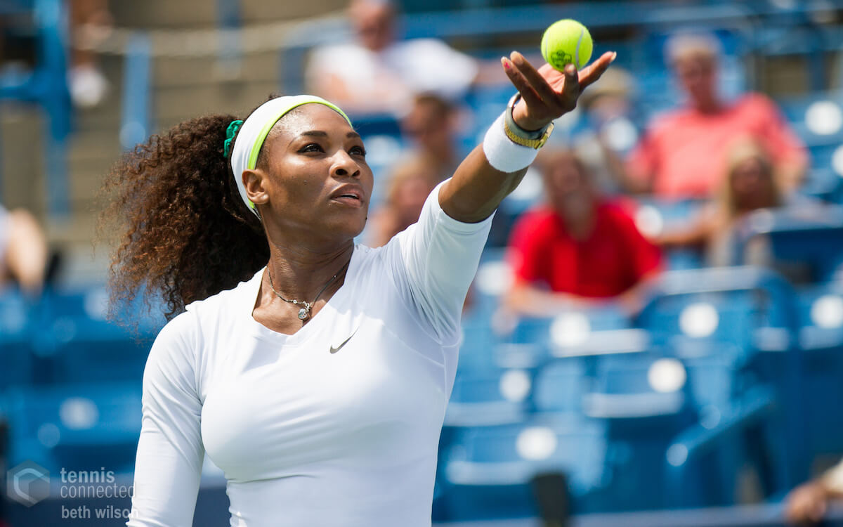 Serena Williams serving a tennis ball on court.